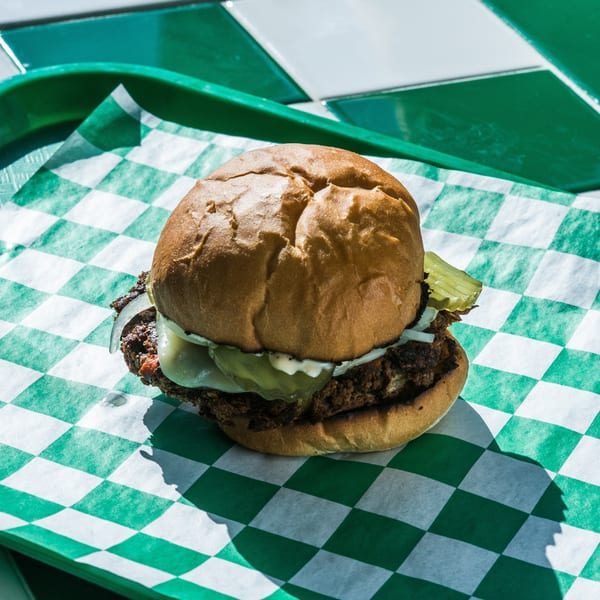 A cheeseburger with pickles and onions on a green and white checkered paper liner.
