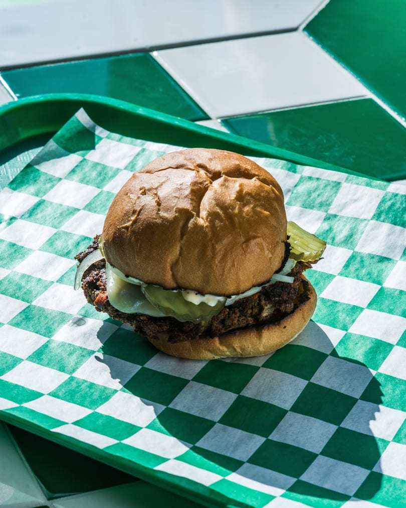 A cheeseburger with pickles and onions on a green and white checkered paper liner.