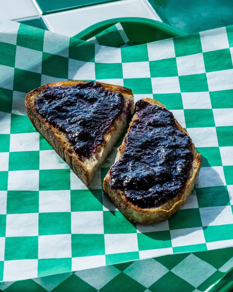 Two slices of toast with dark berry jam on green and white checkered paper.