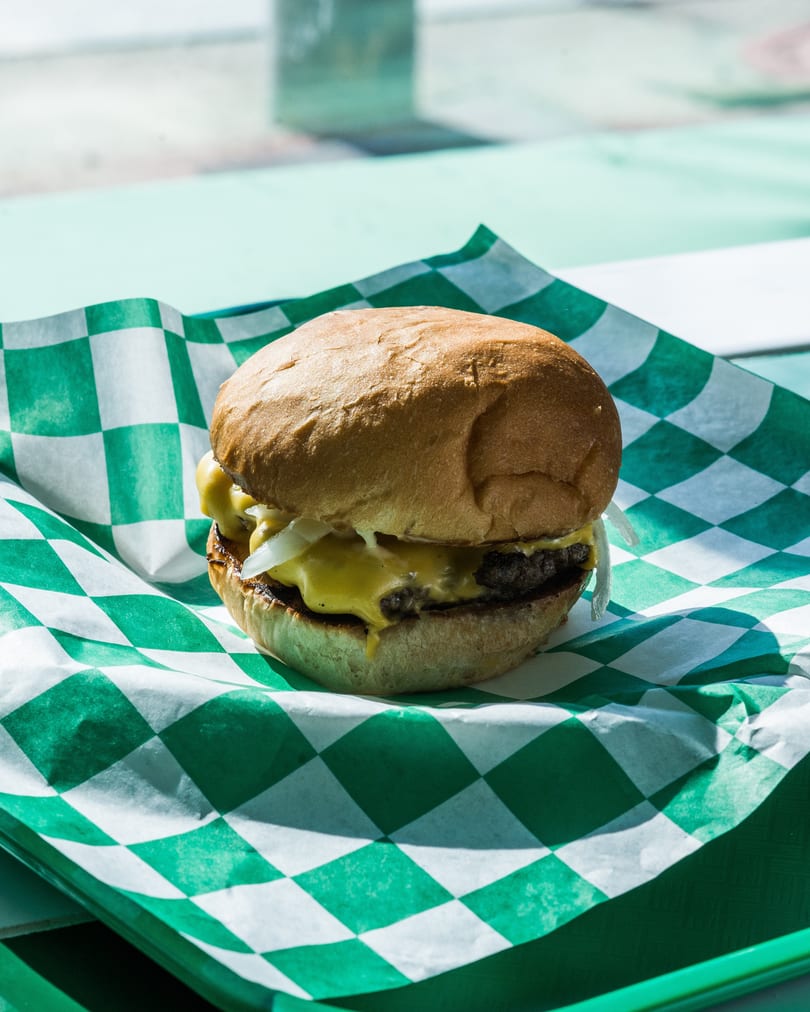 A cheeseburger with melted cheese and onions on a green and white checkered paper liner.
