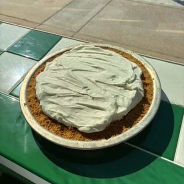 A whole pie with a crumb crust and light green creamy filling sits on a green and white checkered counter.