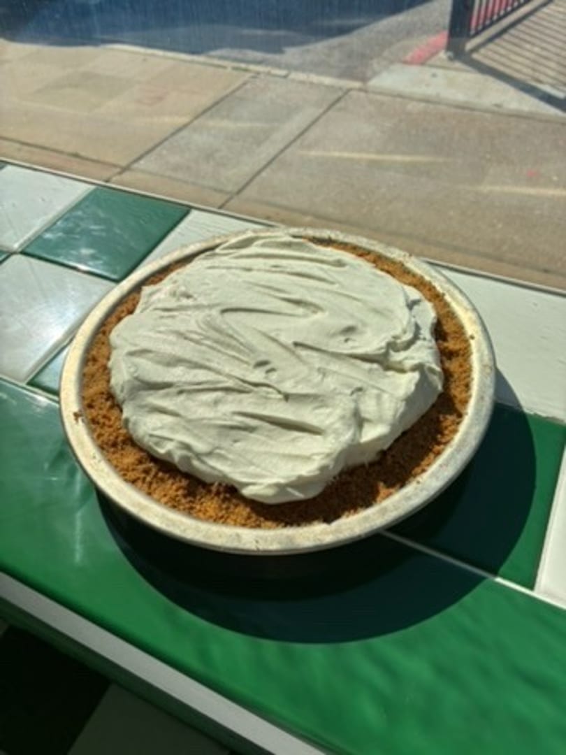 A whole pie with a crumb crust and light green creamy filling sits on a green and white checkered counter.