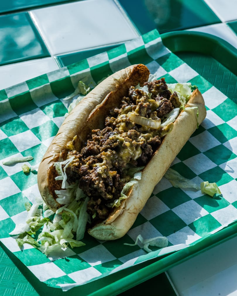 Cheesesteak sandwich with chopped meat, melted cheese, onions, and lettuce on a green checkered tray.