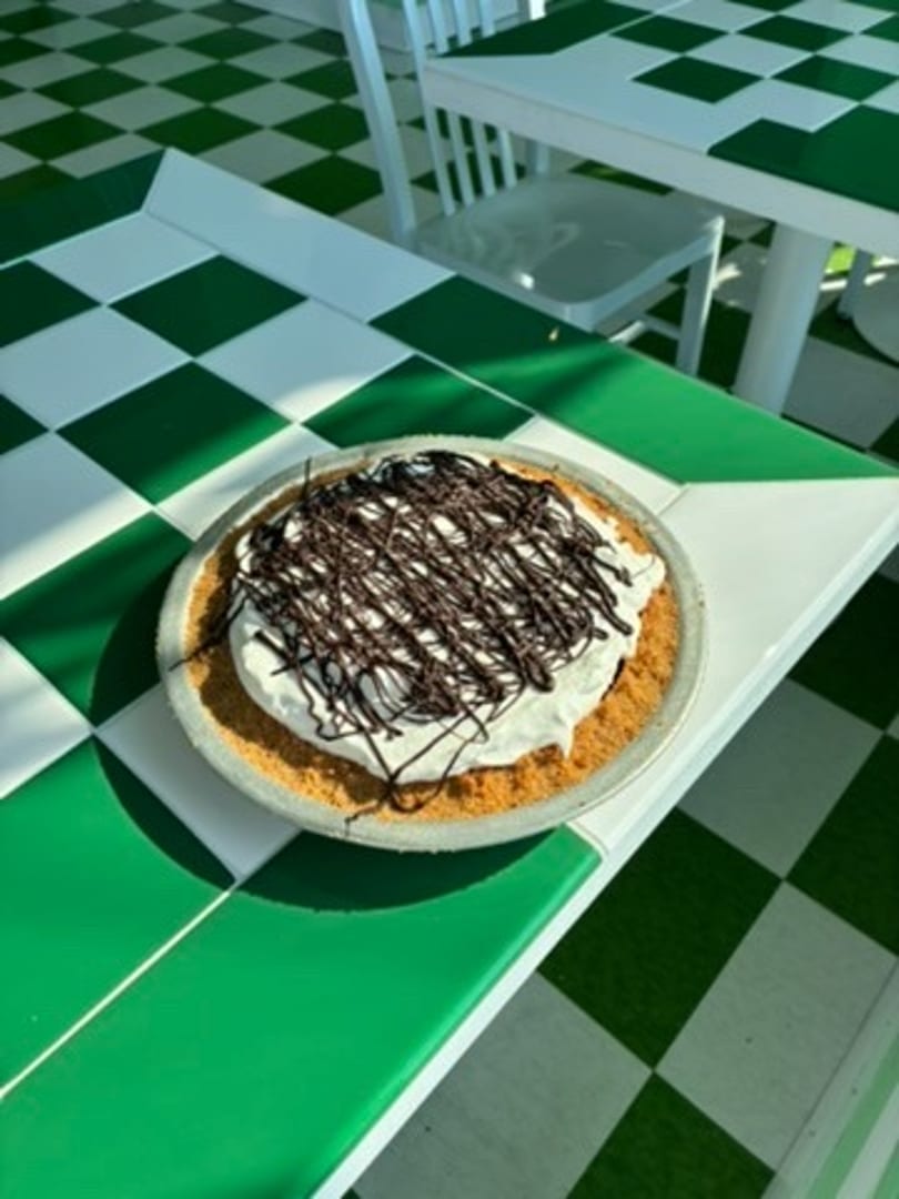 A chocolate drizzled pie with whipped cream on a green and white checkered table.