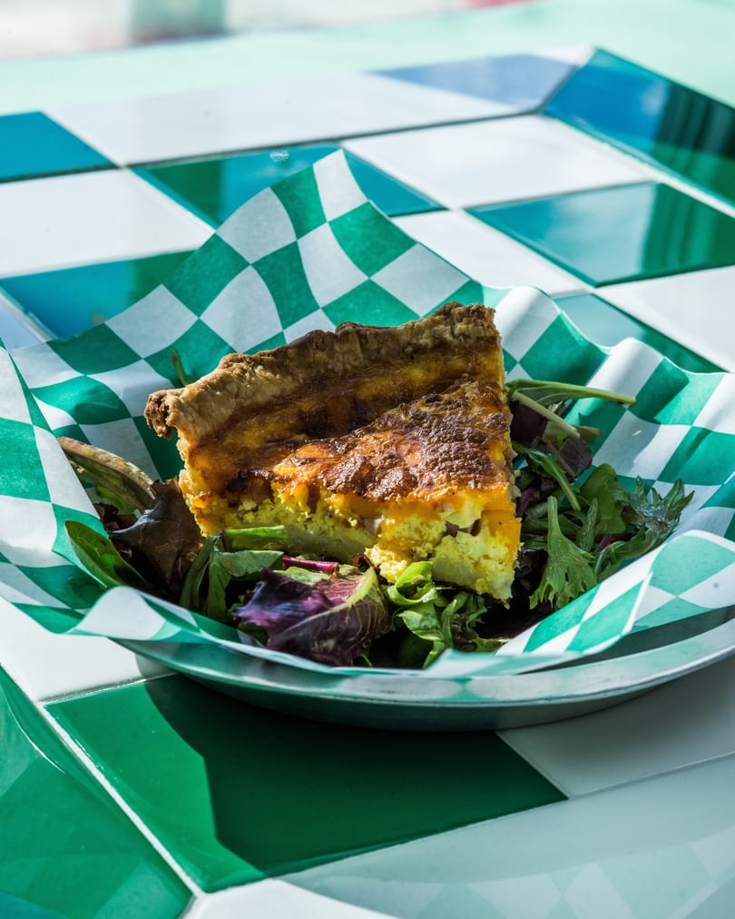 A slice of quiche with a side salad in a green and white checkered paper liner.